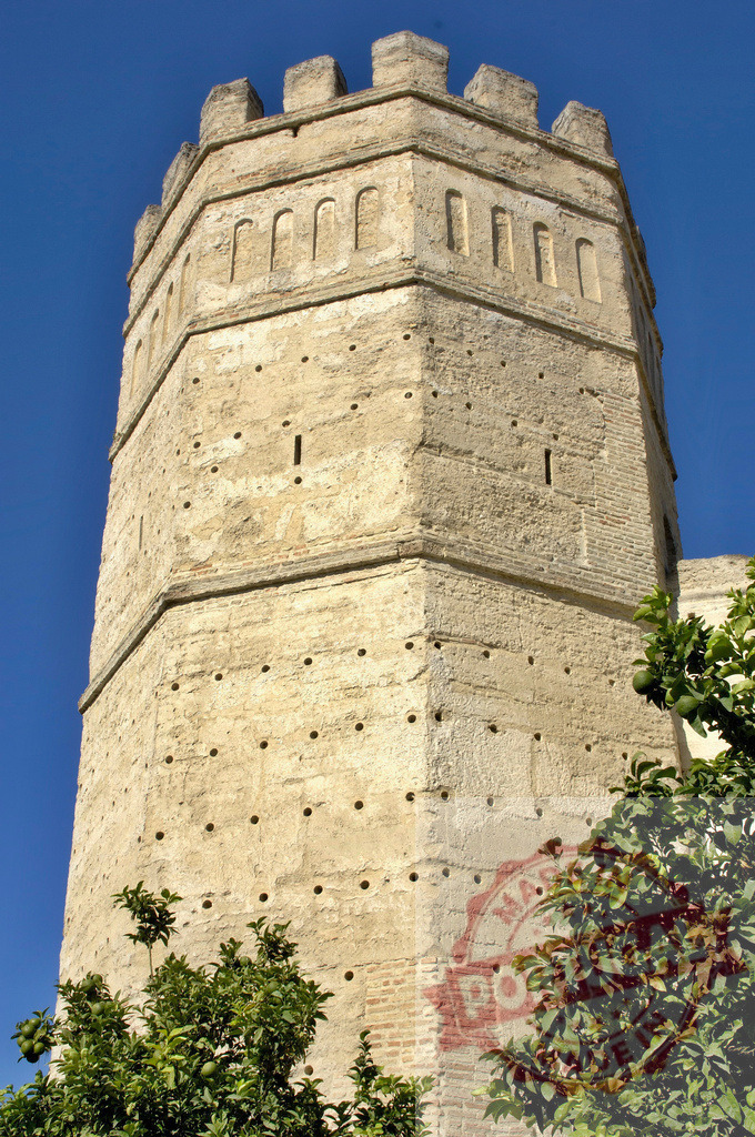 Ancient stone tower with battlements against blue sky. Espana - Cadiz | Historic stone tower from an ancient fortress standing against a clear blue sky - Realisiert mit Pictrs.com