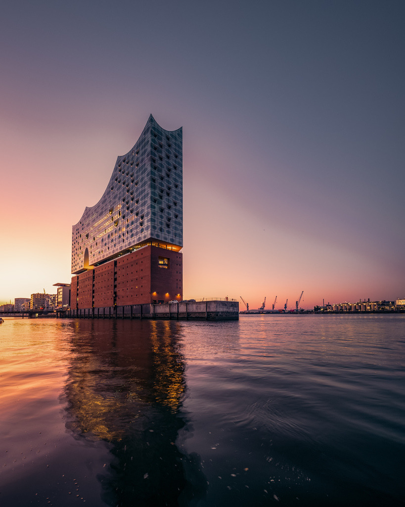 Elbphilharmonie im goldenen Morgenlicht | Die Elbphilharmonie am Hamburger Hafen im warmen Licht des Sonnenaufgangs, gespiegelt im bewegten Wasser der Elbe. - Realisiert mit Pictrs.com