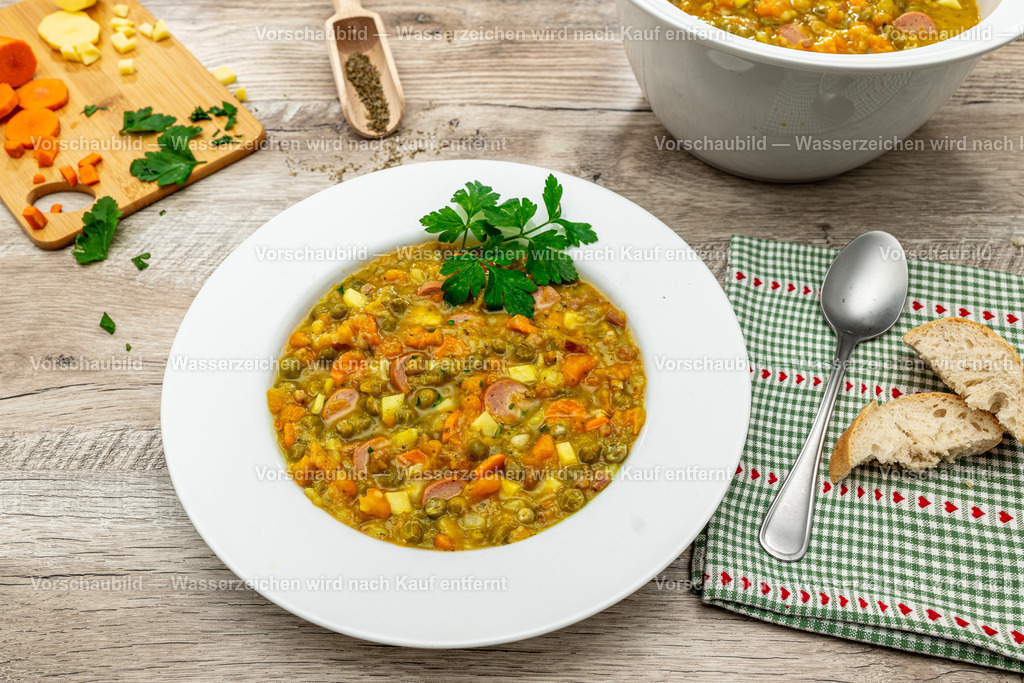 Ein Teller deftige Erbsensuppe | Ein Teller deftige Erbsensuppe, dekoriert mit Brot, Tuch, Besteck, rohes Suppengemüse, und Kräuter - Realisiert mit Pictrs.com