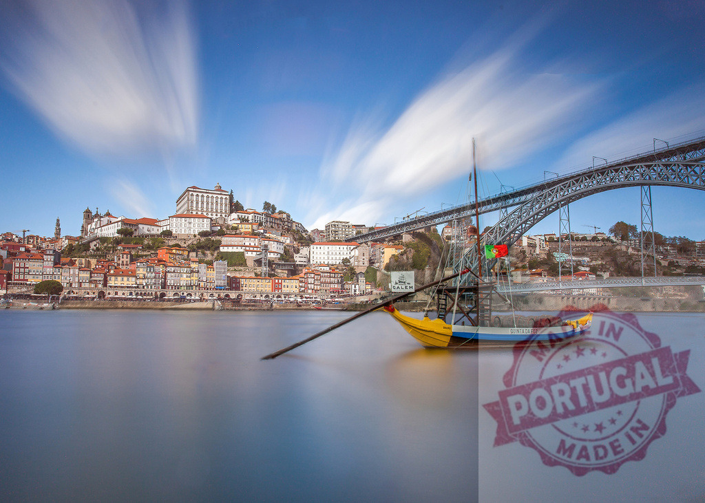 Rabelo boat floating on Douro river, Porto cityscape at sunset | Traditional rabelo boat on the Douro river with Ribeira and Dom Luís I Bridge under a long exposure sky - Realized with Pictrs.com