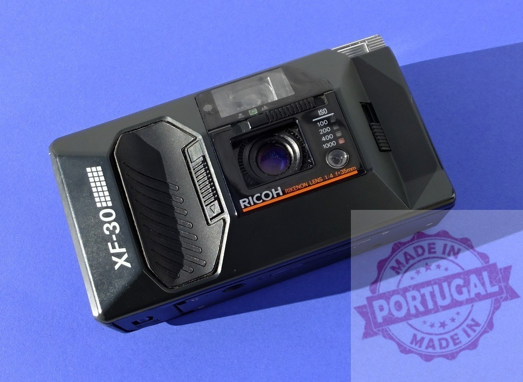 Ricoh XF-30 vintage 35mm film point and shoot camera | Black Ricoh XF-30 film camera on a solid blue background - Realized with Pictrs.com
