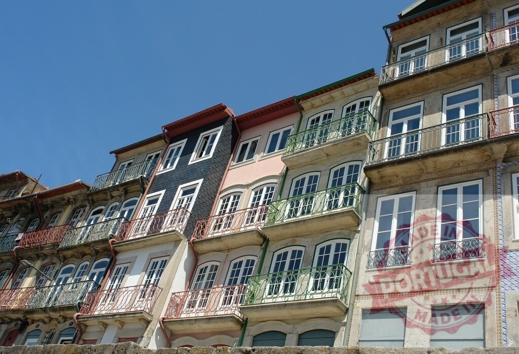 Ribeira District, Porto building facades with balconies under blue sky. Porto - Portugal | Historic buildings with colorful facades and ornate balconies line a street in Porto, Portugal - Realized with Pictrs.com