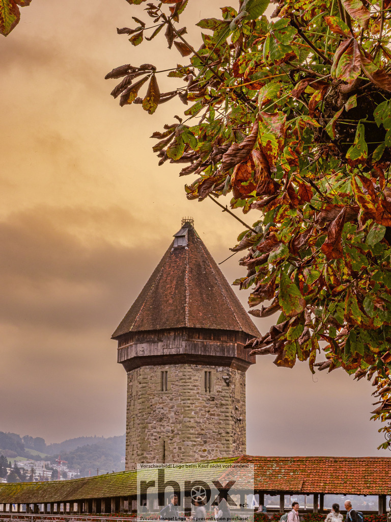 Wasserturm im Herbstlaub | <p><strong>Laub. Turm. Geschichte.</strong></p><p>Eingerahmt von den sich färbenden Blättern der Kastanienbäume steht der historische Wasserturm als unerschütterlicher Zeuge der Zeit. Die warme, fast goldene Lichtstimmung taucht das Luzerner Wahrzeichen in eine Atmosphäre voller Ruhe und Nostalgie.</p><p>Wähle unter "Produktauswahl" dein Wunschformat: Vom klassischen Wandbild über Puzzle & Tassen bis zum digitalen Download (z.B. als Handy-Hintergrund).</p> - Realisiert mit Pictrs.com