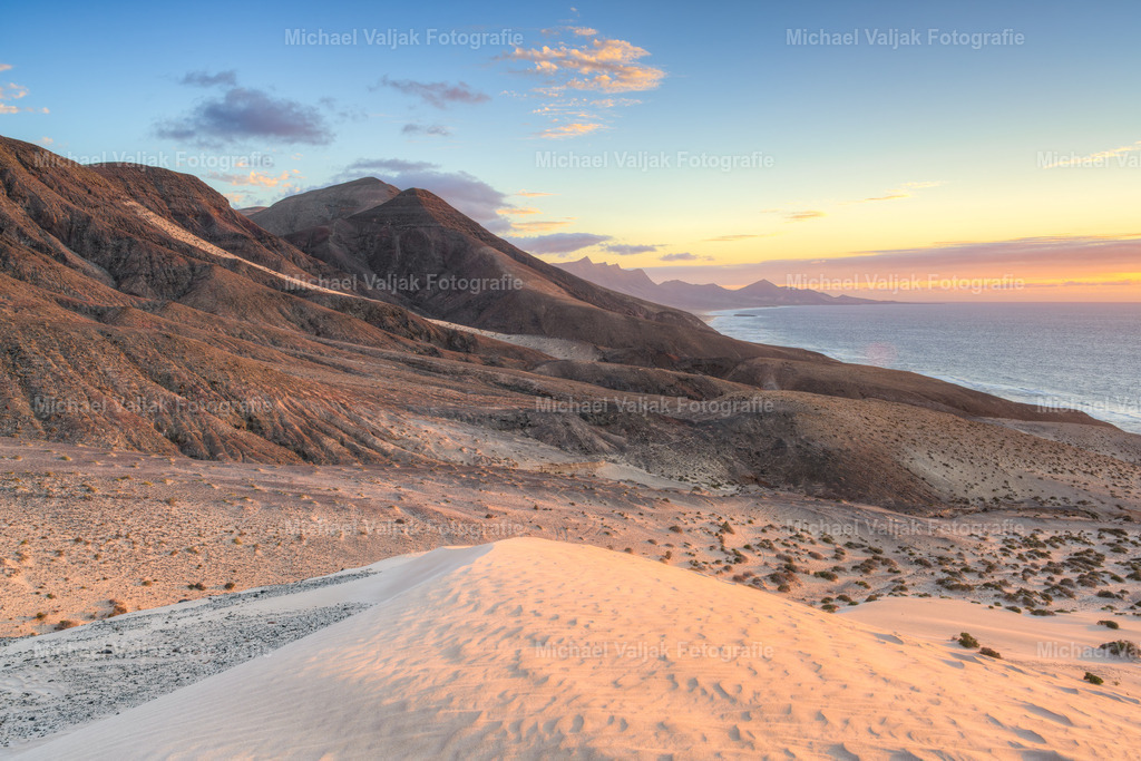 Jandia Fuerteventura | Von den Dünen in Jandía reicht der Blick weit bis zu den südlichen Bergen. Der Sand fällt sanft ab, die Formen wirken ruhig und offen. In der Ferne zeichnen sich die Berge klar gegen den Himmel ab und geben der Landschaft Tiefe. Ein schlichter Moment, der zeigt, wie harmonisch Dünen und Berge hier ineinander übergehen. - Realisiert mit Pictrs.com