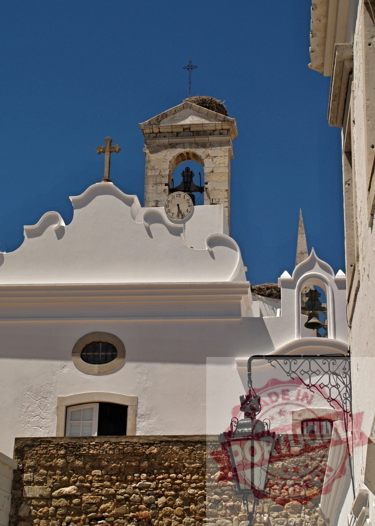 Faro cathedral bell tower with stork nest under blue sky | White church bell tower with a clock and stork nest under a clear blue sky in Faro, Portugal - Realized with Pictrs.com