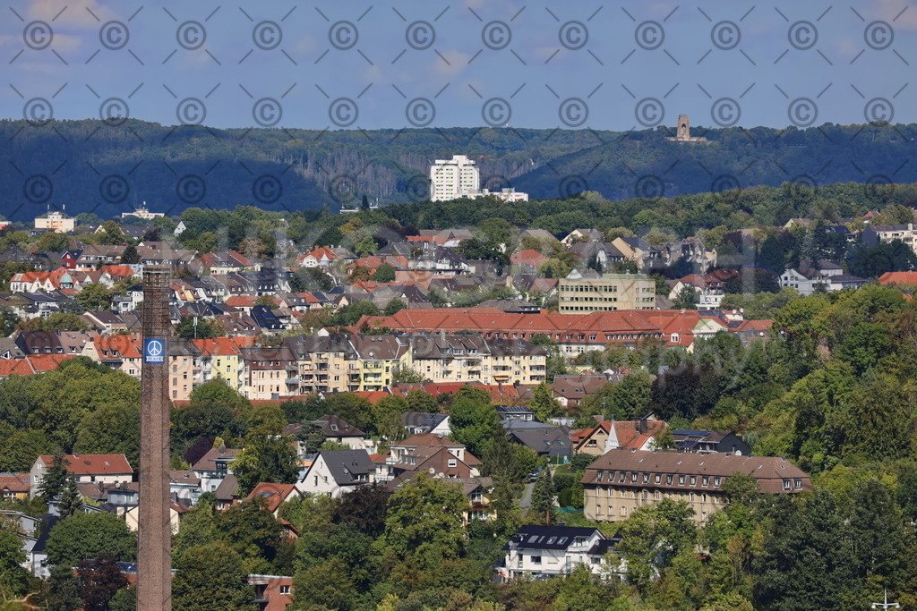 Hagen-Nikograph-18 | Ein Blick in den Norden der Stadt Hagen. Im Vordergrund der Schornstein der Elbershallen, der mit einem Peace-Banner verziert ist. Im Hintergrund ist das Kaiser-Wilhelm-Denkmal zu sehen un ddazwischen diverse Wohnhäuser der Volmemetropole Hagen.