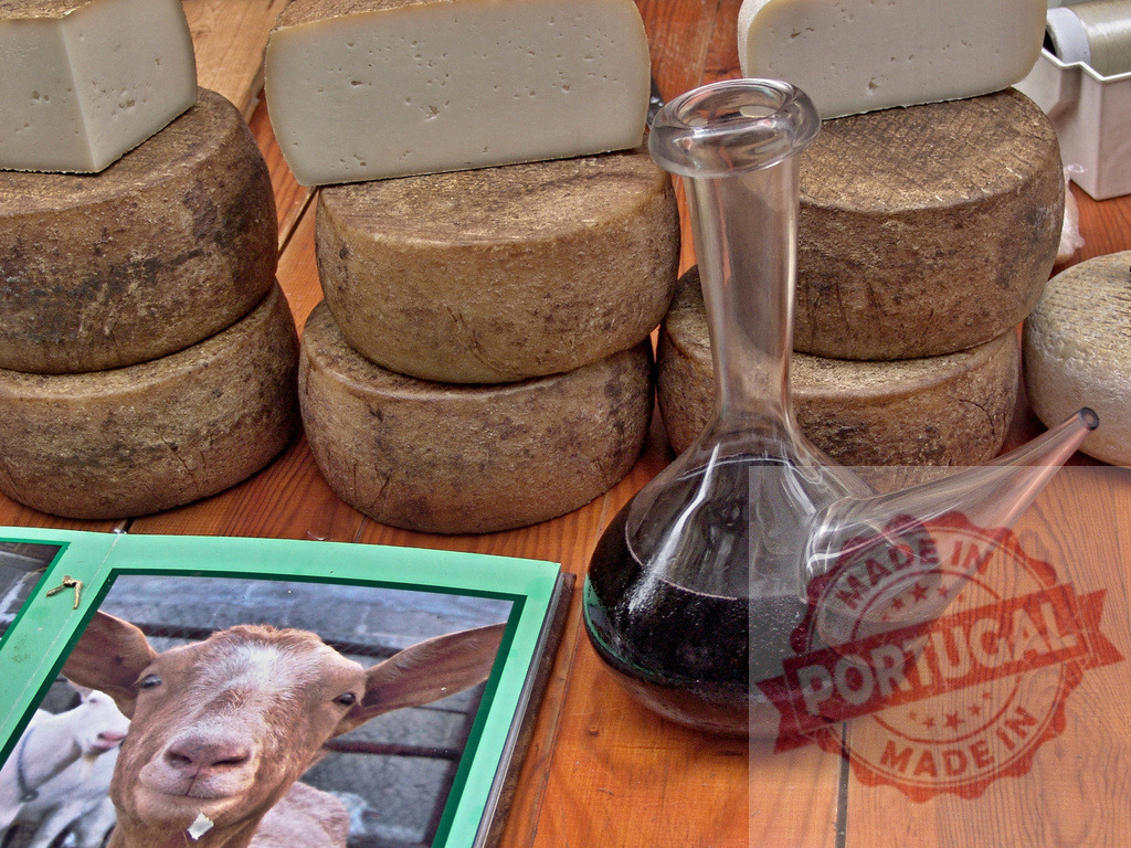 Artisan cheese aging with red wine porrón and goat | Artisan cheese wheels, a porrón of red wine, and a goat image on a rustic wooden table - Realized with Pictrs.com