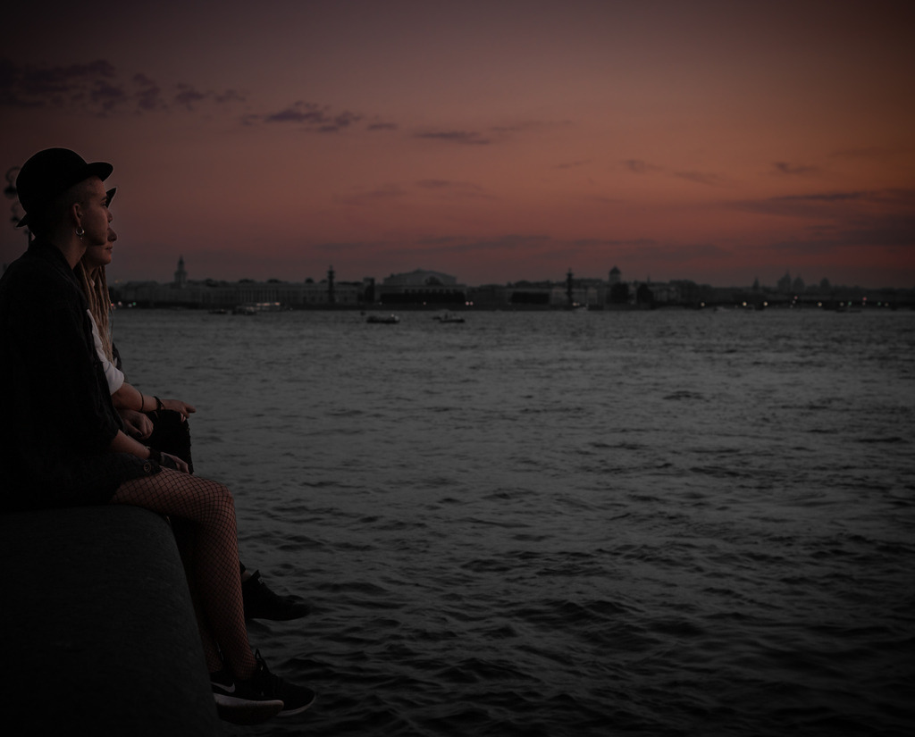 Between Light and Silence | Between light and silence, the gaze drifts toward the horizon of the setting sun. The fading light and the quiet presence of the water create a moment of reflection and calm. The photograph captures a contemplative atmosphere between day and night, where the city slowly fades into stillness. - Realisiert mit Pictrs.com