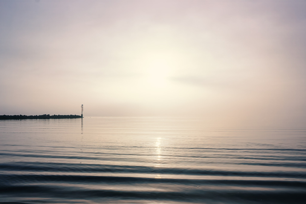 Zeitlose Meeresstille – Helles Wandbild Küstennebel an der Ostsee | Ein sanfter Schleier aus Nebel legt sich über die ruhige See und lässt den Horizont fast gänzlich verschwinden. Das diffuse Licht und die weichen Wellenbewegungen im Vordergrund erzeugen eine Atmosphäre von tiefer Geborgenheit und meditativem Frieden. Die dezente Silhouette der Mole am Rand gibt dem Blick einen sanften Halt, ohne die unendliche Weite der Szenerie zu unterbrechen. Ein edles Motiv, das Ruhe und Besinnlichkeit in jeden Raum trägt.