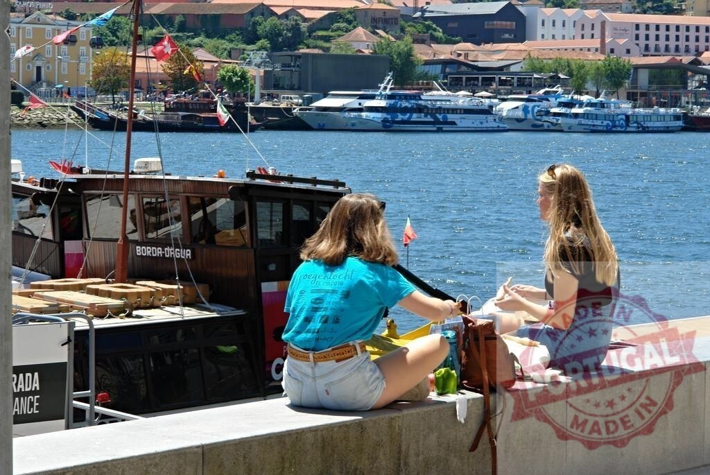 Women relaxing eating lunch by Douro river in Porto. Porto - Portugal | Two young women enjoying a waterfront picnic during summer vacation in Portugal - Realized with Pictrs.com