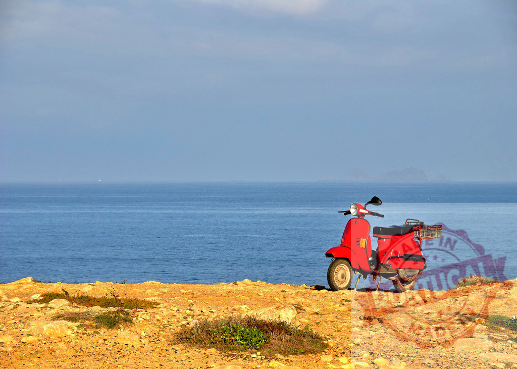 Red vintage scooter parked overlooking Mediterranean sea. Centro Portugal | Red classic scooter parked on a rocky cliffside, ocean and horizon in background - Realized with Pictrs.com