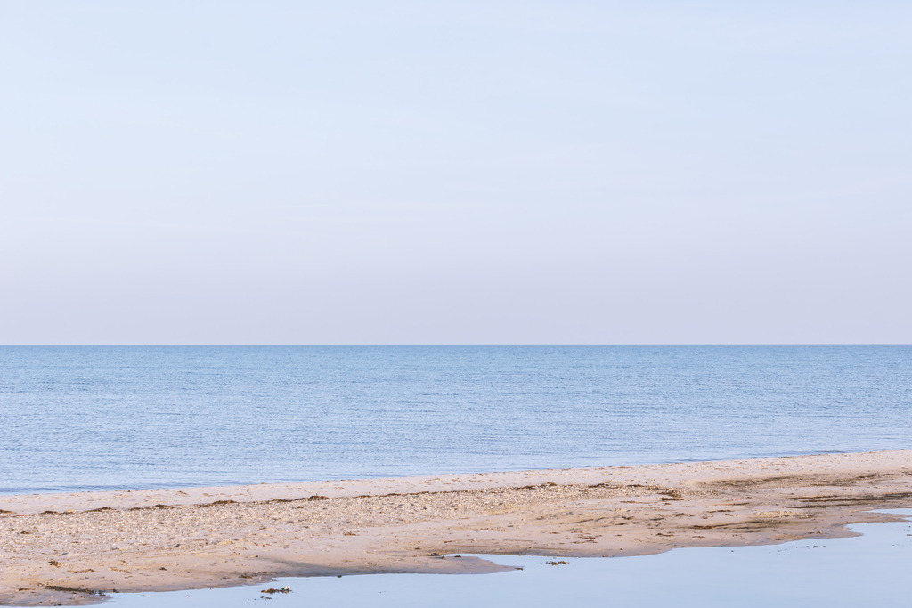 Wandbild: Küstenweite Falshöft - Minimalistischer Sandstrand | Dieses minimalistische Wandbild besticht durch seine elegante Einfachheit und die sanfte Farbästhetik der Ostsee bei Falshöft. Eine schmale Sandbank im Vordergrund trennt das ruhige Uferwasser vom offenen Meer, während der klare Horizont und die zarten Blautöne dem Raum Weite und Atem spenden. Eine stilvolle und beruhigende Fotokunst für moderne Wohnkonzepte.