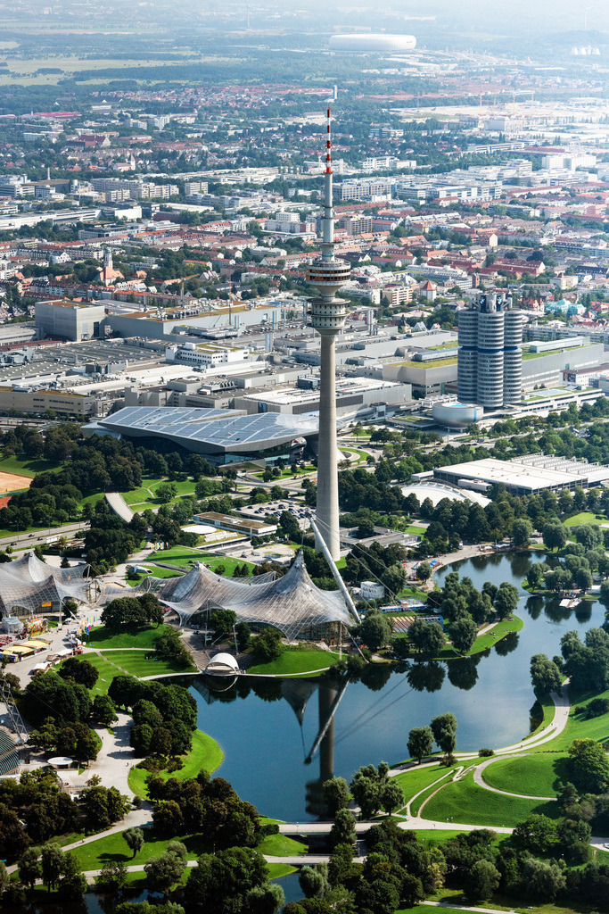 dr__0071261.jpg | MüNCHEN 12.08.2021 Der Olympiapark in München im Bundesland Bayern. Im Vordergrund liegt das Olympiastadion, das heute für Veranstaltungen und Konzerte genutzt wird. Dahinter liegt der Fernsehturm, der Olympiaturm, eines der Wahrzeichen Münchens. Ebenfalls sichtbar ist die Parkanlage sowie der große See. Gemeinsam bilden sie eine der größten Grünflächen der Stadt. // The Olympic Park in Munich in the state of Bavaria. In the foreground lies the Olympic Stadium that is today used for cultural events and concerts. Behind it, the TV tower, the Olympic Tower, one of the landmarks of the city is visible. The large park and lake form one of the largest open spaces in Munich. Foto: Daniel Reiter
