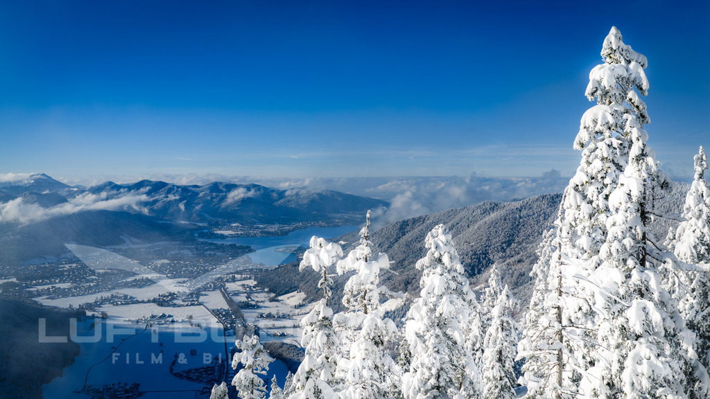 Gruß von der Rinnerspitz gen Rottach: Jennerweins Fundort; W48 | Ein weiter Wintergruß von der Rinnerspitz hinab ins Tegernseer Tal: Tief verschneite Bäume stehen im Vordergrund, während sich dahinter der Tegernsee und Rottach-Egern in klarer Luft ausbreiten. Hier, wo einst der Jennerwein seine Spuren hinterließ, verbindet sich eindrucksvolle Natur mit einem Hauch Geschichte – ein kraftvoller Moment zwischen Himmel, Schnee und weitem Blick. - Realisiert mit Pictrs.com