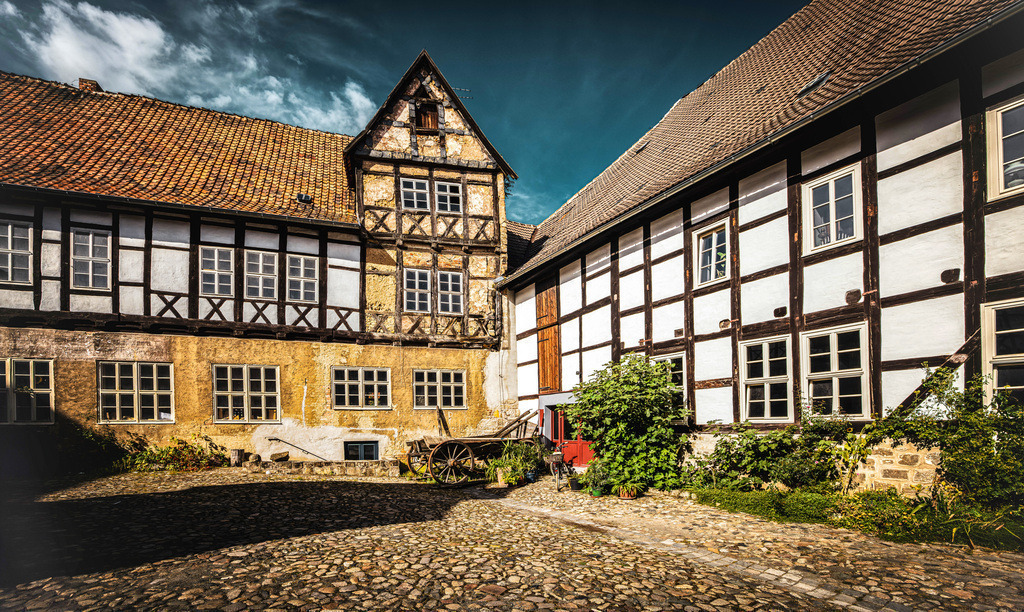 Blick in einen mittelalterlichen Innenhof in Quedlinburg | Das Bild zeigt einen Innenhof mit historischen Fachwerkhäusern in der Altstadt von Quedlinburg. Quedlinburg ist eine UNESCO-Welterbestadt am Nordrand des Harzes. Die Stadt ist bekannt für ihren riesigen Bestand von über 2000 Fachwerkhäusern aus verschiedenen Jahrhunderten. Die mittelalterliche Altstadt zeichnet sich durch verwinkelte Gassen und idyllisches Kopfsteinpflaster aus. Die Region bietet zahlreiche Sehenswürdigkeiten wie den Münzenberg, das Schloss und den Domschatz.  - Realisiert mit Pictrs.com