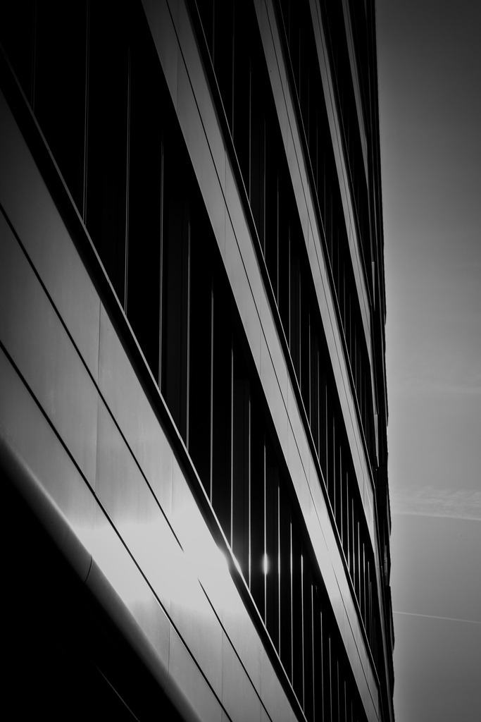 Modern Architecture Lines – Black and White Urban Fine Art Photography | Black and white fine art photograph of modern urban architecture at Duisburg Innenhafen, Germany. The minimalist composition emphasizes strong geometric lines, contrast and light reflections on the building facade, creating a modern architectural fine art image with a clean urban aesthetic. - Realisiert mit Pictrs.com