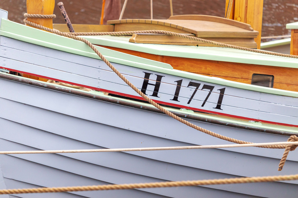 Wandbild: Boot im Hafen | Dieses Wandbild im Querformat zeigt ein Boot im Ostseehafen. Im Vordergrund hängen Seile. - Realisiert mit Pictrs.com