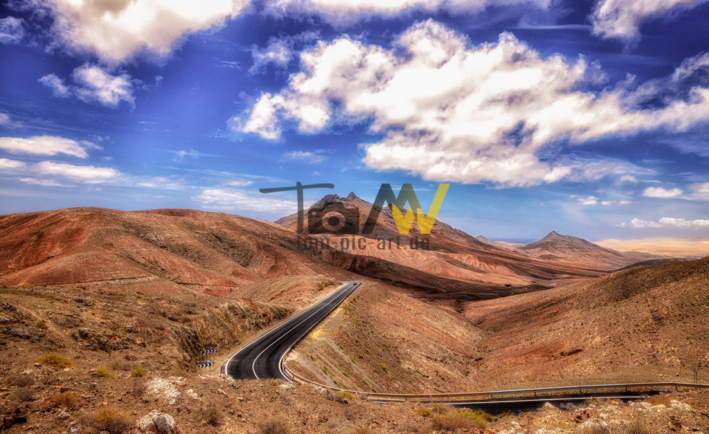 Blick über die sanften Hügel--Landschaft von Fuerteventura | Viele Straßen wurden zum Zeitpunkt der Aufnahme neu geteert. Schlängeln sich kurvenreich durch die sanften Hügelketten Fuerteventuras. Blauer Himmel, blick soweit das Auge reicht... - Realisiert mit Pictrs.com