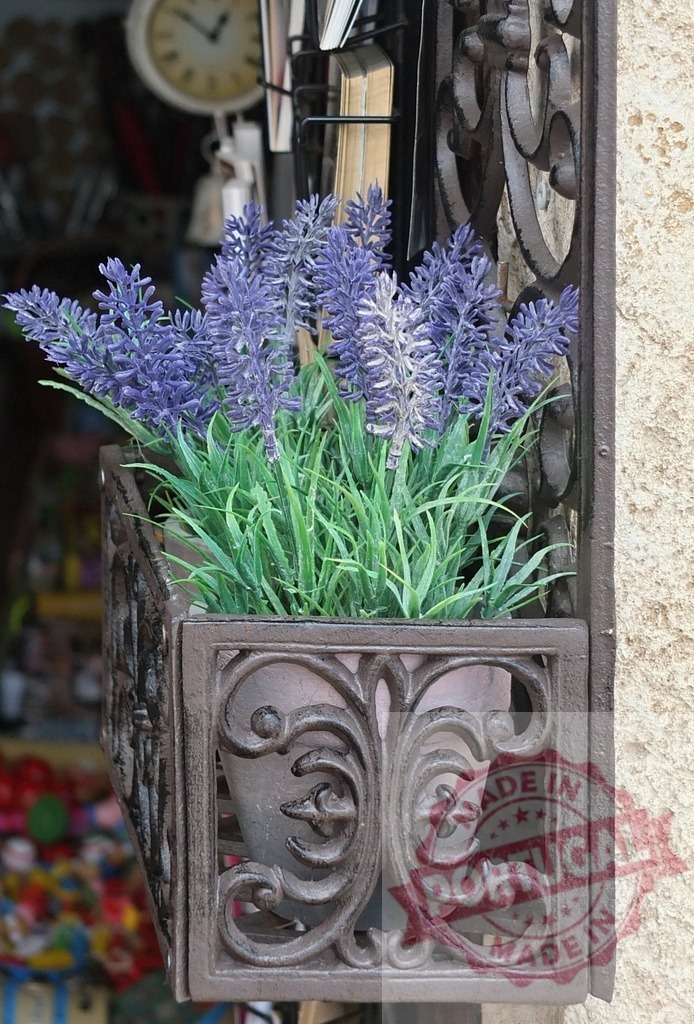 Purple faux lavender plant in vintage metal window planter | Faux lavender flowers blooming in an ornate cast iron window box garden planter - Realized with Pictrs.com