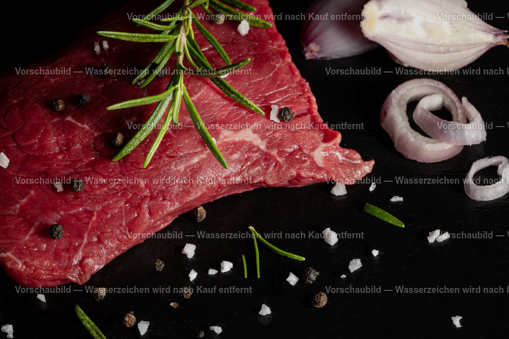 rohes Rinder Hüftsteak auf schwarzer Schieferplatte angerichtet | rohes Rinder Hüftsteak auf schwarzer Schieferplatte angerichtet. Dekoriert mt einen Zweig Rosmarien, Pfefferkörnern, Schalotten und groben Salz - Realisiert mit Pictrs.com