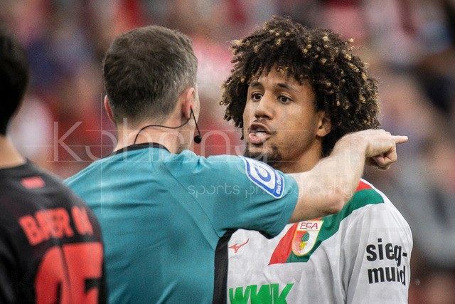 German Bundesliga, Bayer 04 Leverkusen vs. FC Augsburg, 18.04.2026 | LEVERKUSEN, GERMANY - APRIL 18, 2026 :  Han-Noah Massengo (FC Augsburg, 4) in discussions with referee Benjamin Brand (Schwebheim) during the German Bundesliga match on gameday 30 between Bayer 04 Leverkusen vs. FC Augsburg at BayArena on April 18, 2026 in Leverkusen, Germany. DFL REGULATIONS PROHIBIT ANY USE OF PHOTOGRAPHS AS IMAGE SEQUENCES AND/OR QUASI-VIDEO.