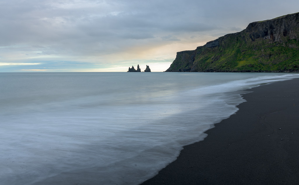 island-2019-255 | Die Bucht von Vík í Mýrdal im Süden Islands im Licht eines Abends im Juni. Im Hintergrund ragen die Basaltfelsen Reynisdrangar, das Wahrzeichen des Ortes, aus dem Meer empor. - Realisiert mit Pictrs.com