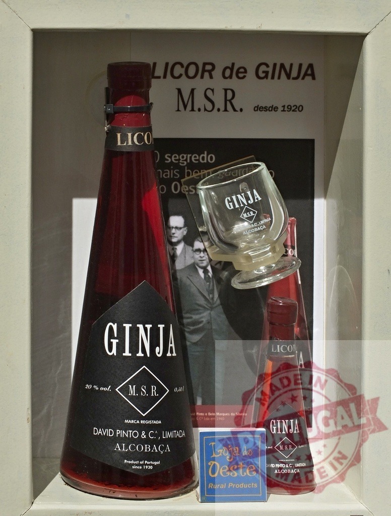 Ginja M.S.R. Cherry liqueur bottles on display | Ginja M.S.R. Cherry liqueur bottles and glass with informational background on a shelf - Realisiert mit Pictrs.com