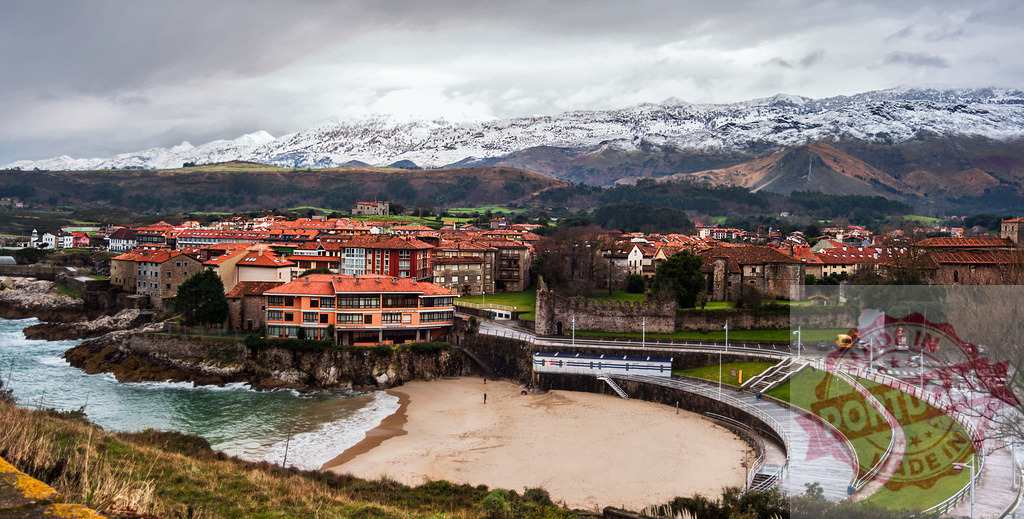 Scenic coastal town of Llanes nestled between snow-capped Picos de Europa mountains and Cantabrian Sea | Picturesque view of Llanes, Spain, showcasing its unique architecture, sandy beach, and the majestic backdrop of the snow-covered Picos de Europa - Realisiert mit Pictrs.com