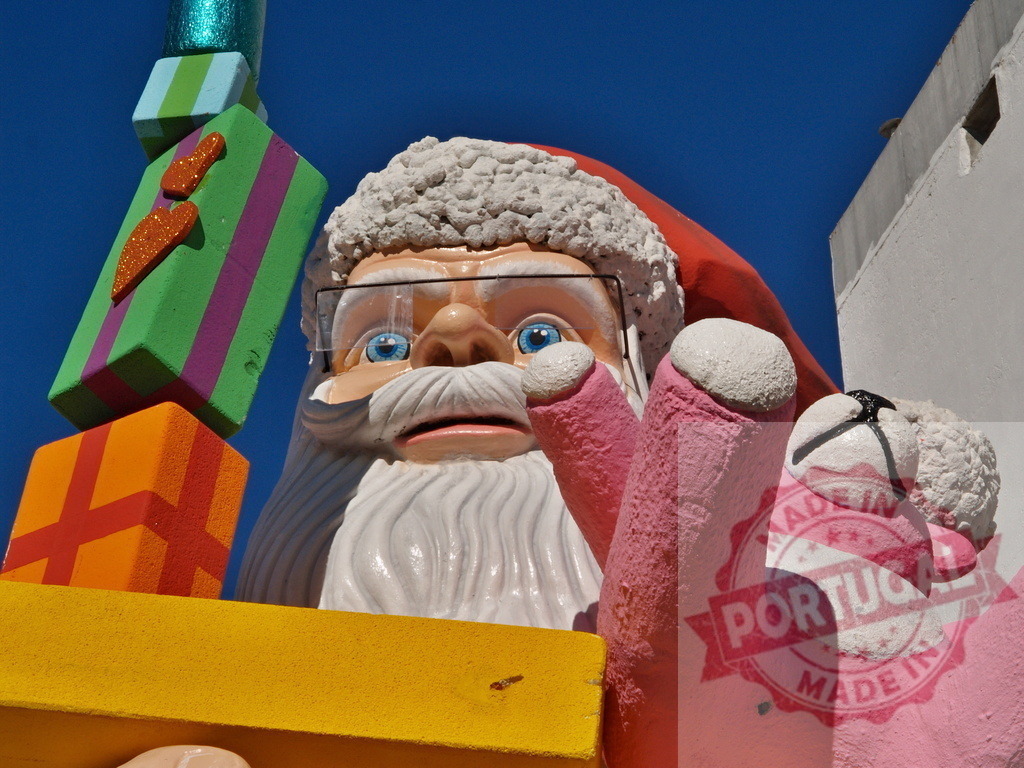 Giant santa claus statue holding pink teddy bear and colorful gifts | Low angle view of a giant santa claus statue holding a pink teddy bear and colorful gifts against a blue sky - Realisiert mit Pictrs.com
