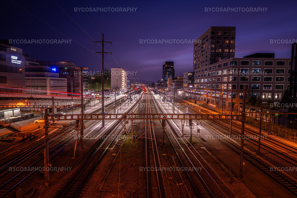 Zürich Tracks _ Night Motion | Eine dynamische Langzeitbelichtung zeigt die im Nachthimmel leuchtenden Bahnstrecken Zürichs. Weiße und rote Lichtstrahlen erzeugen Bewegung und Energie, während moderne Stadtviertel und ein violett-blauer Himmel dem Bild Eleganz und eine futuristische Atmosphäre verleihen.Dieser Druck eignet sich perfekt für moderne Wohnungen, Büros, Coworking-Spaces und alle, die Architektur und Stadtplanung lieben. - Realisiert mit Pictrs.com