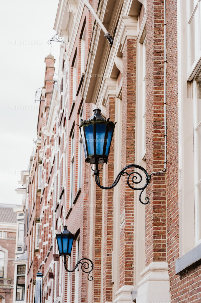 blaue Leuchte | Eine kunstvoll geschmiedete Laterne mit blauem Glas an einer schönen städtischen Ziegelwand im Tageslicht. Das Bild zeigt urbanen Charme und handwerkliche Details – perfekt als Kunstdruck für besondere Raumgestaltungen. - Realisiert mit Pictrs.com