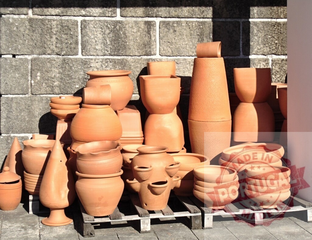 Terracotta clay pots and ceramic garden containers | Various pottery items displaying craftsmanship on a wooden pallet against a stone wall - Realized with Pictrs.com