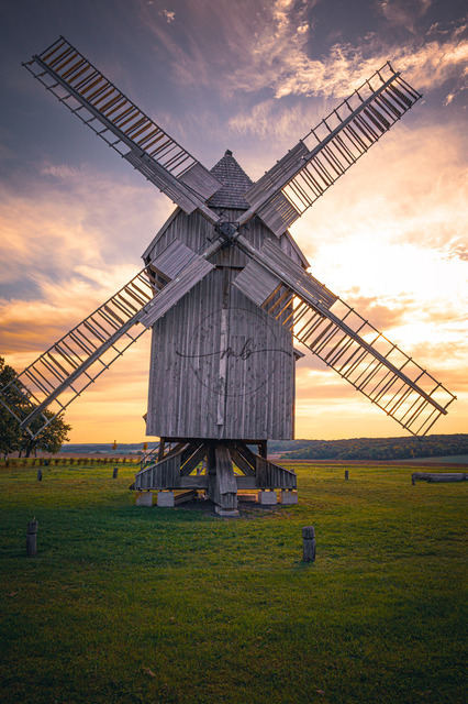 Bockwindmühle bei Sonnenaufgang auf grüner Wiese | Bockwindmühle bei Sonnenaufgang auf grüner Wiese, umgeben von natürlicher Idylle
