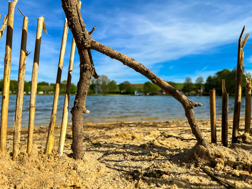 Seefort - Gedern | Die Farbenpracht um den Gederner See erwacht zu neuem Leben. Mit gelben Ockertönen schmiegt der Sand sich um die bloßen Zehen. Während das blau-klare Wasser sanft an die Uferränder pocht, regt sich die üppige Vegetation mit saftigem Grün. Die Bienen und Hummeln brummen schwarz-gelb gestreift von Knospe zu Knospe und auch die Menschen kehren mit ihrer unendlichen Farbenvielfalt zurück in die sanfte Badebucht. - Realisiert mit Pictrs.com