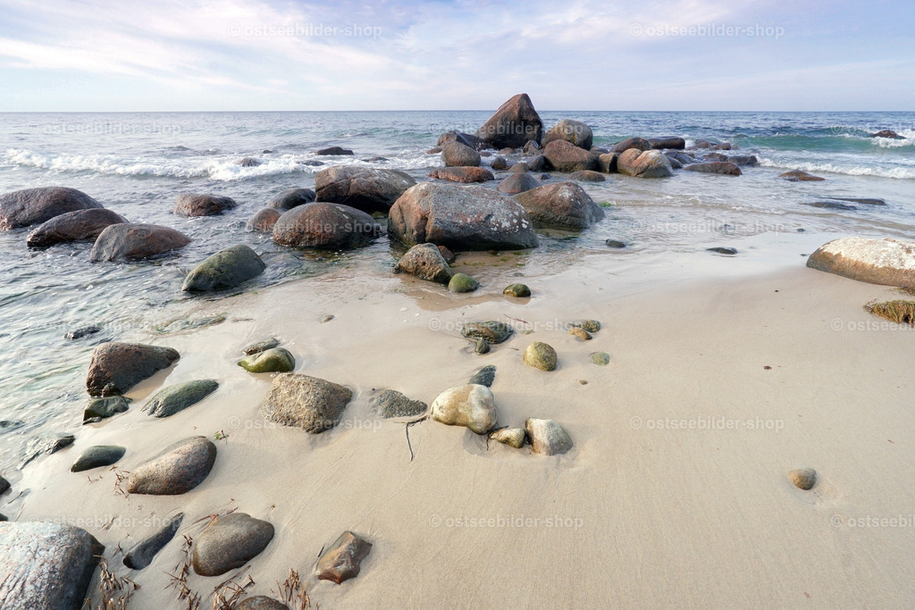 Sand und Steine | Steine liegen am Ostseeufer halb im flachen Wasser und halb im glatten Sand.