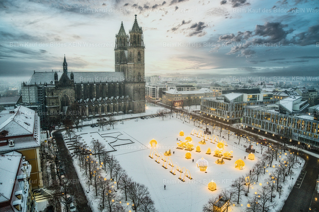 Lichterwelt-0045-2 | Magdeburgs historisches Herz im winterlichen Lichterglanz: Diese atemberaubende Luftaufnahme aus der Vogelperspektive zeigt den komplett verschneiten Domplatz in der Landeshauptstadt Magdeburg. Neben der mächtigen Silhouette des Magdeburger Doms St. Mauritius und Katharina erstrahlt das kunstvolle Ensemble der Magdeburger Lichterwelt im warmen LED-Glanz. Die Riesen-Weihnachtskugeln, Lichterbögen und historischen Großskulpturen setzen leuchtende Akzente auf der makellosen, weißen Schneedecke. Der weite Blick reicht über die winterliche City und fängt die einzigartige, friedliche Atmosphäre der Ottostadt perfekt ein. Ein meisterhaftes und hochgradig repräsentatives Heimatmotiv, das sich ideal als edles Wandbild auf Alu-Dibond oder Acrylglas für Wohn- und Geschäftsräume eignet sowie für das anspruchsvolle regionale Standortmarketing lizenziert werden kann. - Realisiert mit Pictrs.com