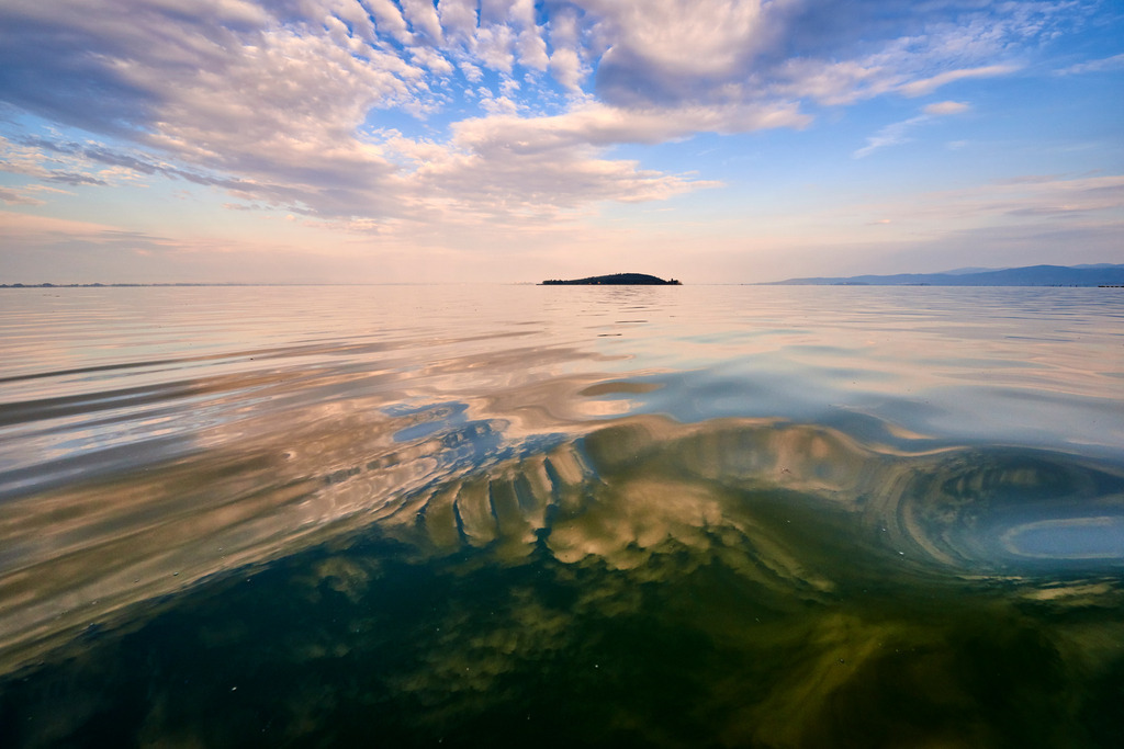 Insel im Morgenlicht | San Feliciano, Italien - August 31, 2016: Lago Trasimeno; eine kleine Insel im Morgenlicht, die Wolken spiegeln sich im Wasser. - Realisiert mit Pictrs.com