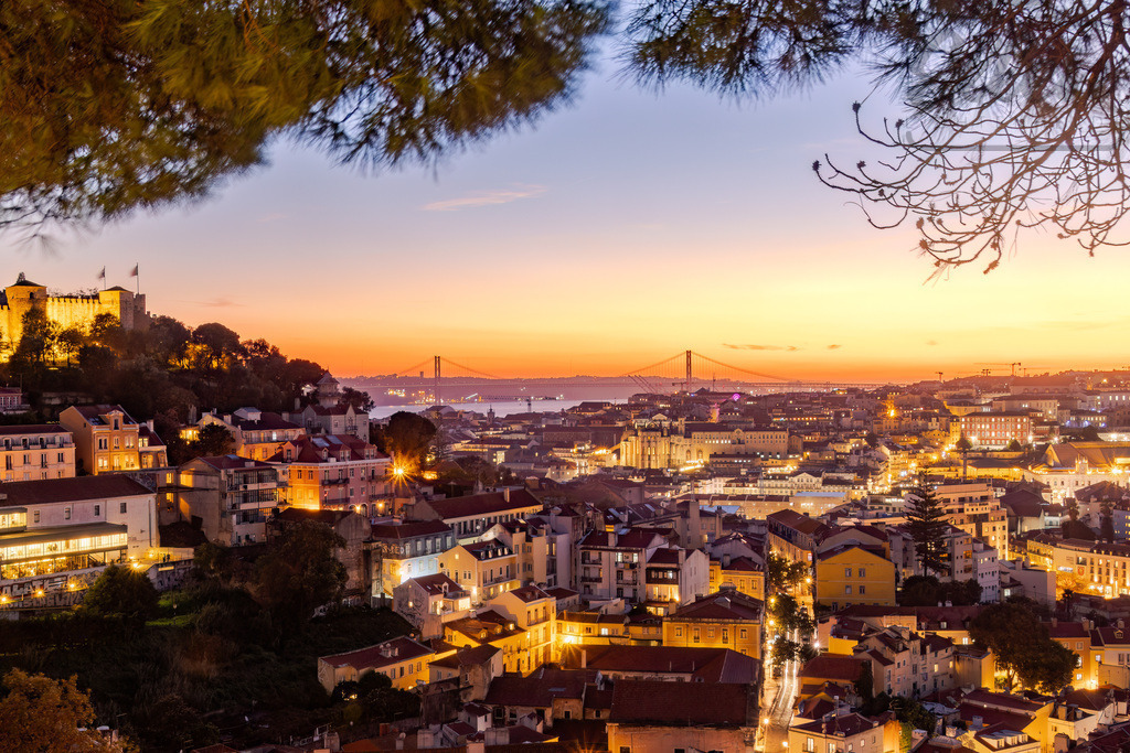 City of Golden Dreams | As daylight fades, Lisbon glimmers between river and sky. The 25 de Abril Bridge and São Jorge Castle glow in harmony, reflecting the city’s timeless rhythm between past and present. - Realisiert mit Pictrs.com