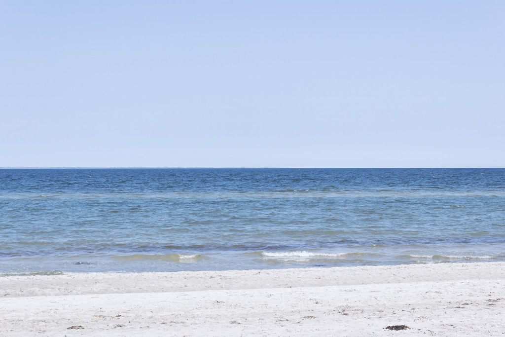 Wandbild: Unendliche Weite - Strand von Falshöft | Dieses elegante Wandbild fängt die zeitlose Schönheit der Ostsee in ihrer reinsten Form ein. Der feine Sandstrand im Vordergrund geht harmonisch in die sanften Farbnuancen des Meeres über und öffnet den Blick für den weiten Horizont. Durch die minimalistische Komposition und die kühlen, beruhigenden Blautöne bringt das Kunstwerk ein Gefühl von Gelassenheit, Balance und purer Küstenfrische in repräsentative Räume – ideal für einen modernen, stilvollen Einrichtungsstil.