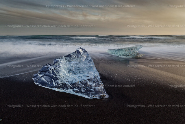 Eis am schwarzen Strand | Blau schimmernde Eisstücke liegen auf dem schwarzen Vulkanstrand Islands, während die Brandung weich im Hintergrund verläuft. Der Kontrast aus klarem Eis, dunklem Sand und bewegtem Meer erzeugt eine stille, kraftvolle und fast surreal wirkende Landschaftsstimmung. - Realisiert mit Pictrs.com