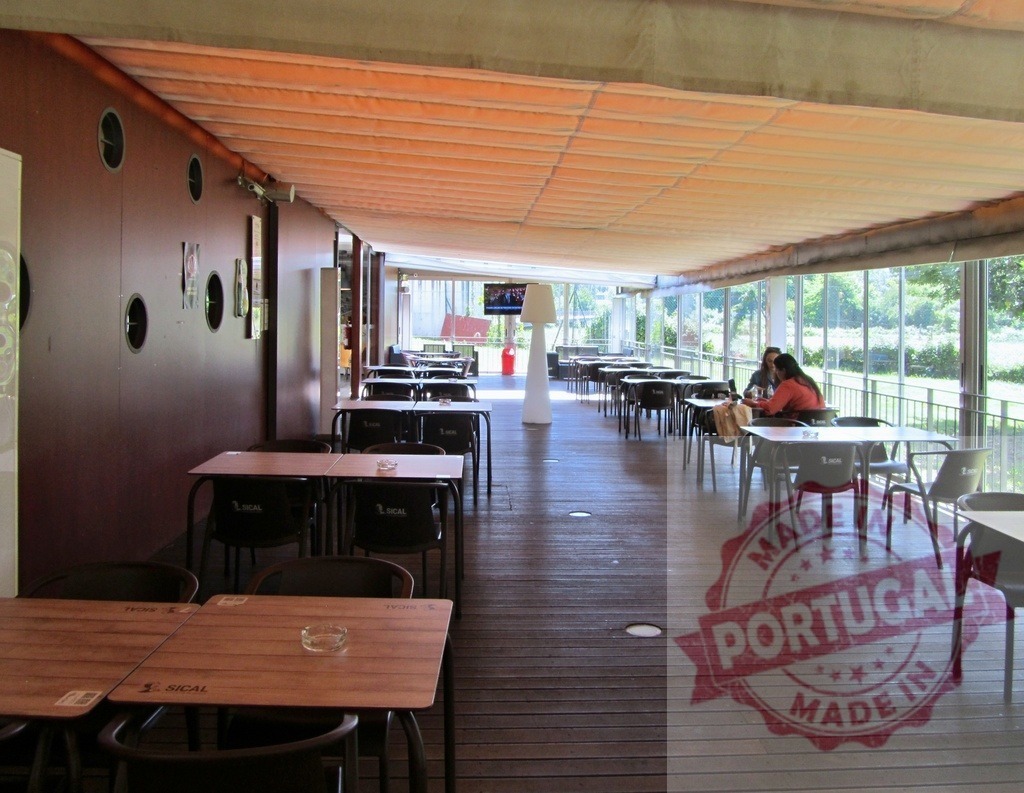 Outdoor cafe terrace with few people relaxing | Outdoor cafe terrace with brown wooden deck, many tables and chairs, and a few people relaxing - Realisiert mit Pictrs.com
