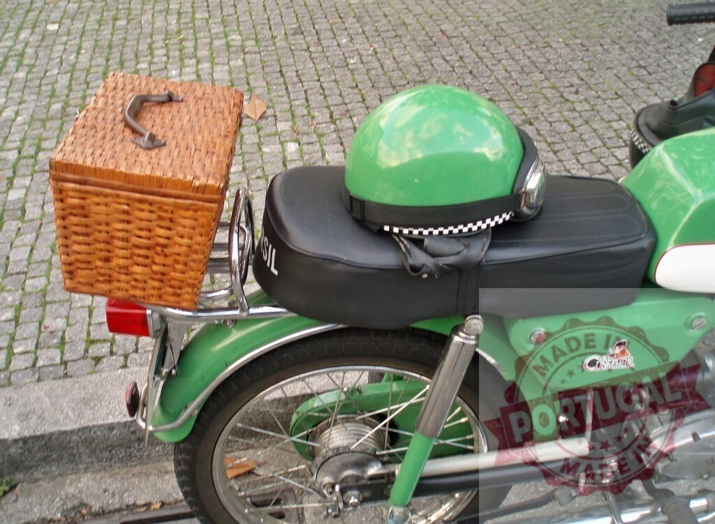 Green motorcycle with wicker basket and helmet parked on cobblestone street | Classic green motorcycle with wicker basket and helmet parked on a cobblestone street, evoking a vintage travel aesthetic - Realisiert mit Pictrs.com