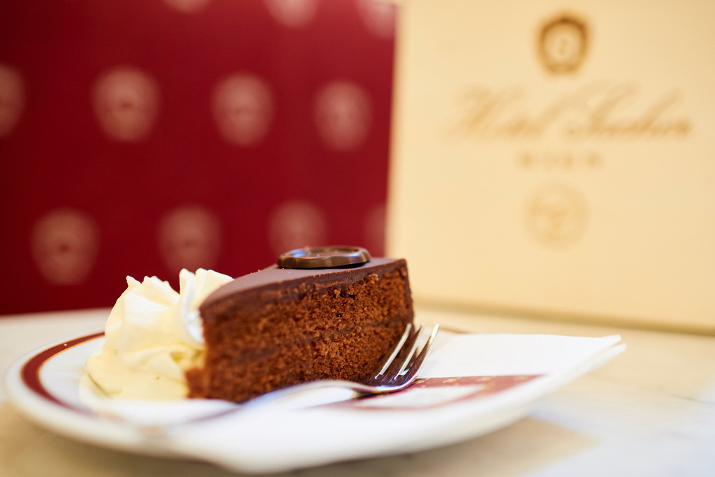 Sachertorte mit Schlagsahne | Wien, Austria - August 22, 2017: Café Sacher, Sachertorte und Melange, im Hintergrund eine Torten-Verpackung. - Realisiert mit Pictrs.com