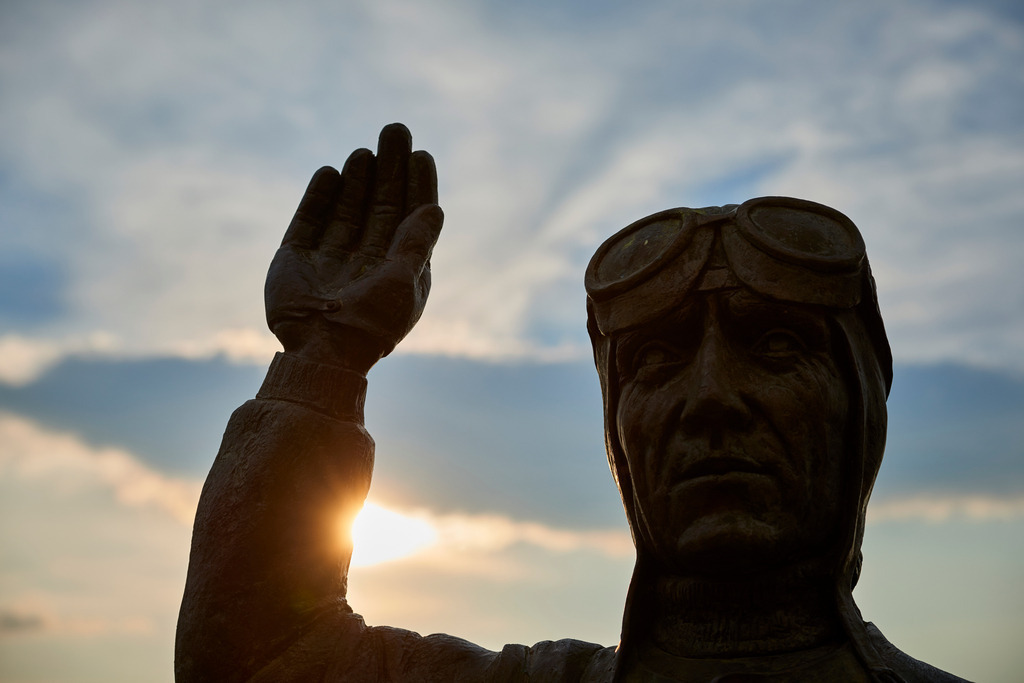 Rennfahrer Tazio Nuvolari Statue | San Quirico d’Orcia, Italien - September 07, 2016: Tazio Nuvolari Rennfahrer Statue im Gegenlicht. - Realisiert mit Pictrs.com