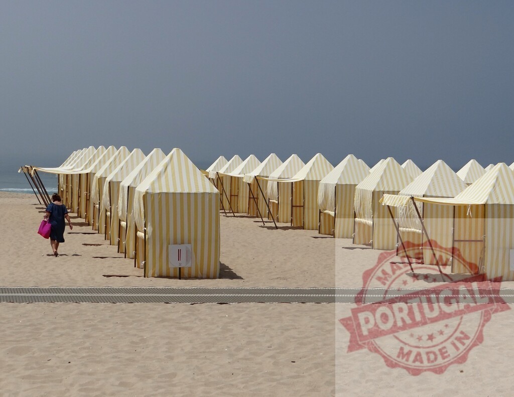 Person walking along beach with rows of striped cabanas | Person walking past yellow striped beach huts on a sandy coastline - Realisiert mit Pictrs.com