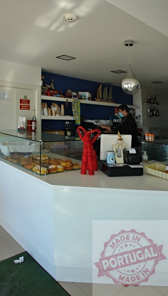 Employee with face mask serving pastries in a bright cafe | Employee wearing a face mask serving food at a cafe counter filled with pastries - Realized with Pictrs.com