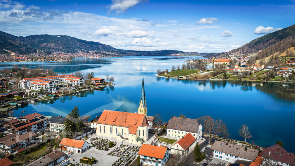 Der Rottacher Malerwinkel (Perspektivwechsel); F21 | Der Rottacher Malerwinkel zeigt sich hier aus einer besonderen Perspektive: Der Blick schweift über das ruhige Wasser des Tegernsees, vorbei an der markanten Kirche und hinein in die sanft geschwungene Landschaft rund um Rottach-Egern. Ein Moment, der die Harmonie aus Natur, Architektur und Weitblick einfängt und einmal mehr zeigt, warum dieser Ort zu den schönsten Motiven im Tegernseer Tal zählt. - Realisiert mit Pictrs.com