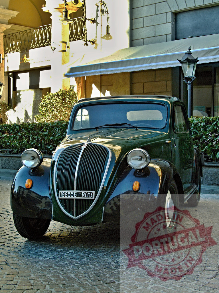 Vintage Fiat 500 Topolino parked in front of a building | Dark green vintage Fiat 500 Topolino parked on a cobblestone street in front of a building - Realized with Pictrs.com