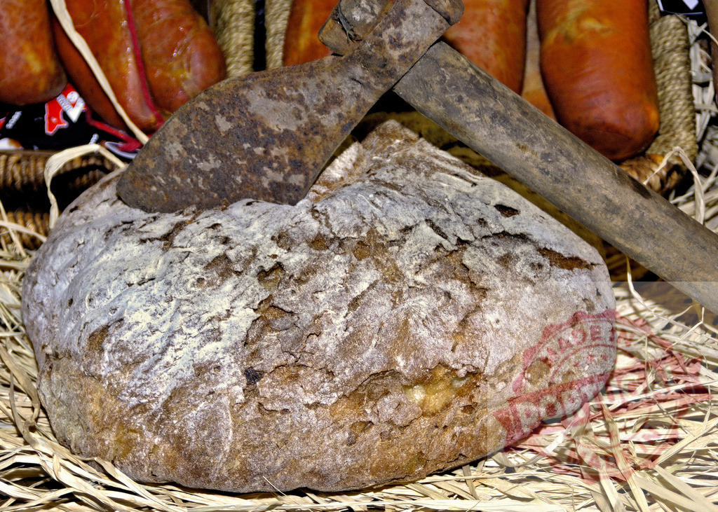 Artisan bread loaf with rustic axe and sausages | Artisan bread loaf with a rusty axe laying on hay, surrounded by traditional sausages - Realisiert mit Pictrs.com