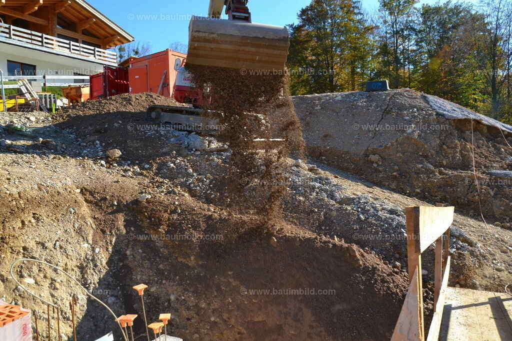 Hinterfüllung Baugrube | Bagger beim Schütten von Schottermaterial in Arbeitsraum 